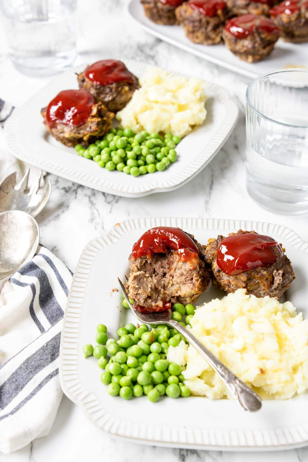 a table with two plates full of meatloaf muffins, peas and mashed potatoes