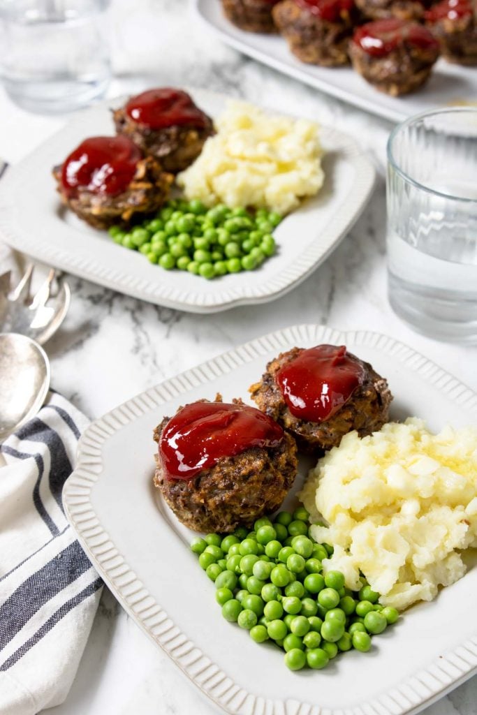 Two plates with meatloaf muffin cups, peas and mashed potatoes