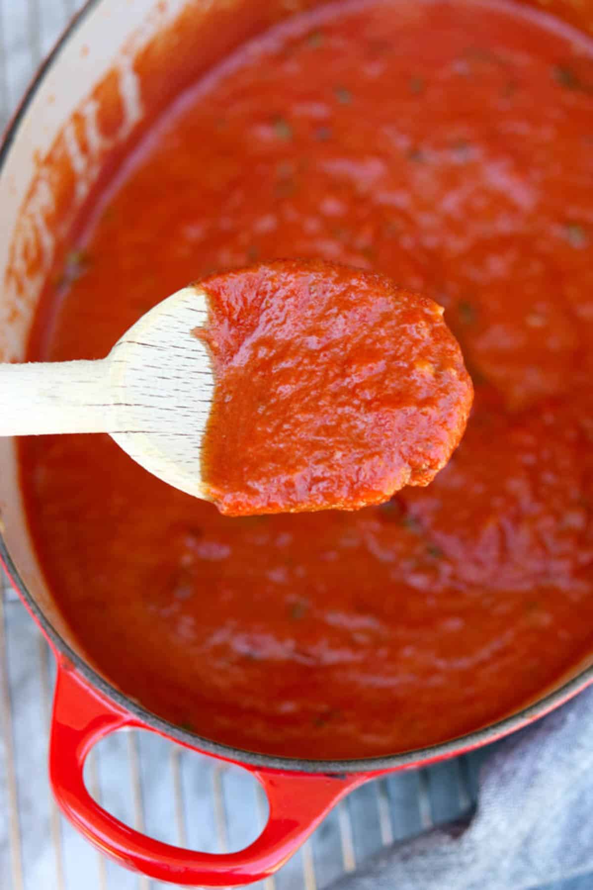 a dutch oven full of marinara sauce with a wooden spoon