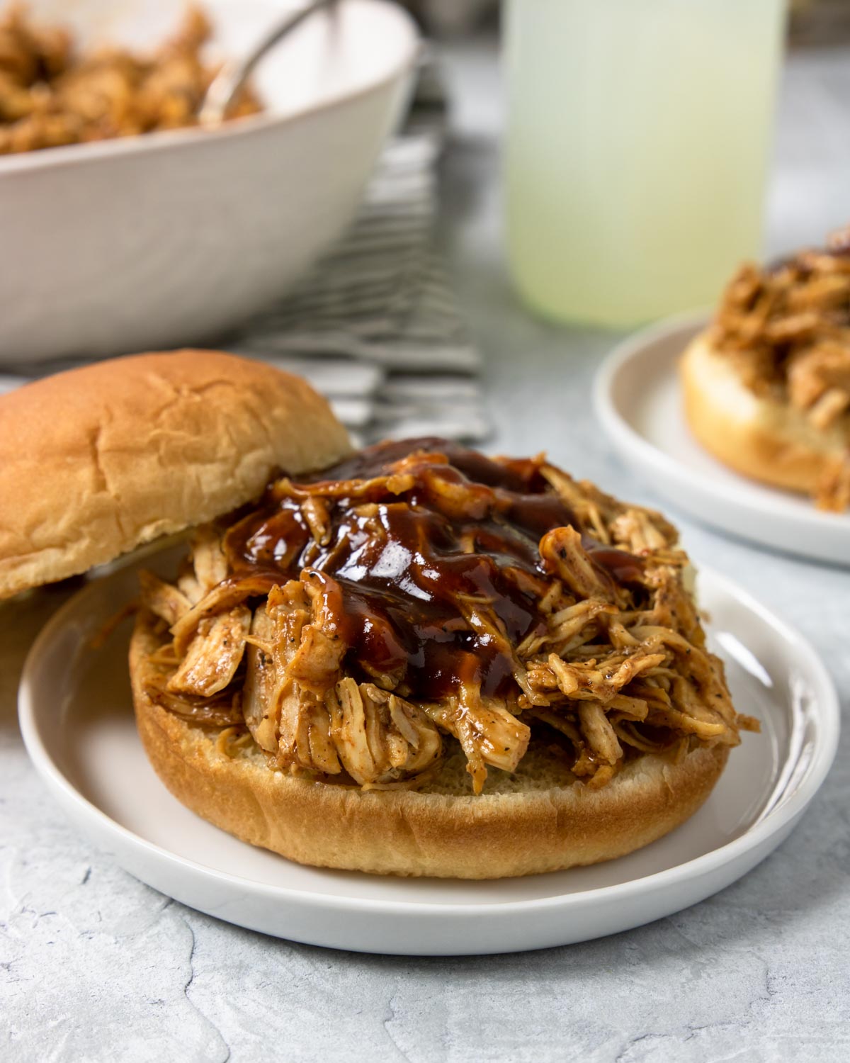 Instant Pot BBQ Chicken Sandwich on a white plate with lemonade in the background