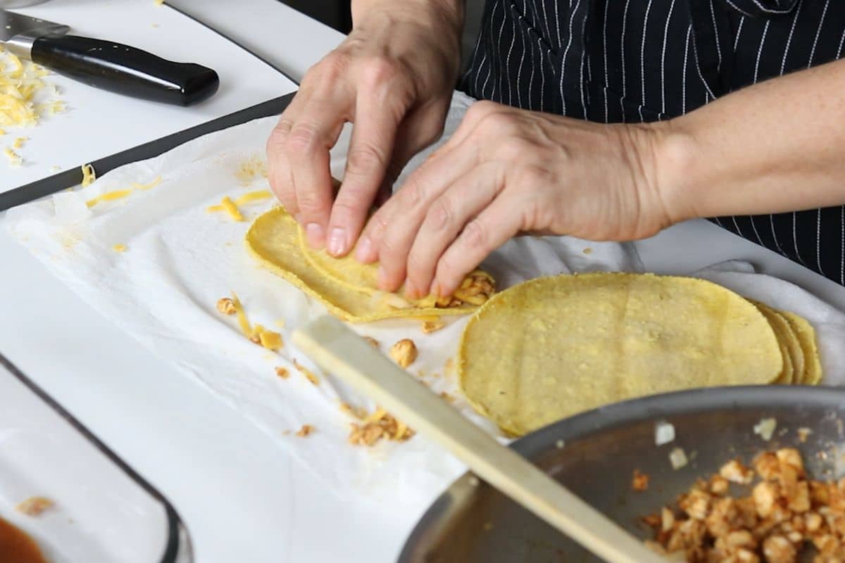 rolling a corn tortilla over enchilada filling 