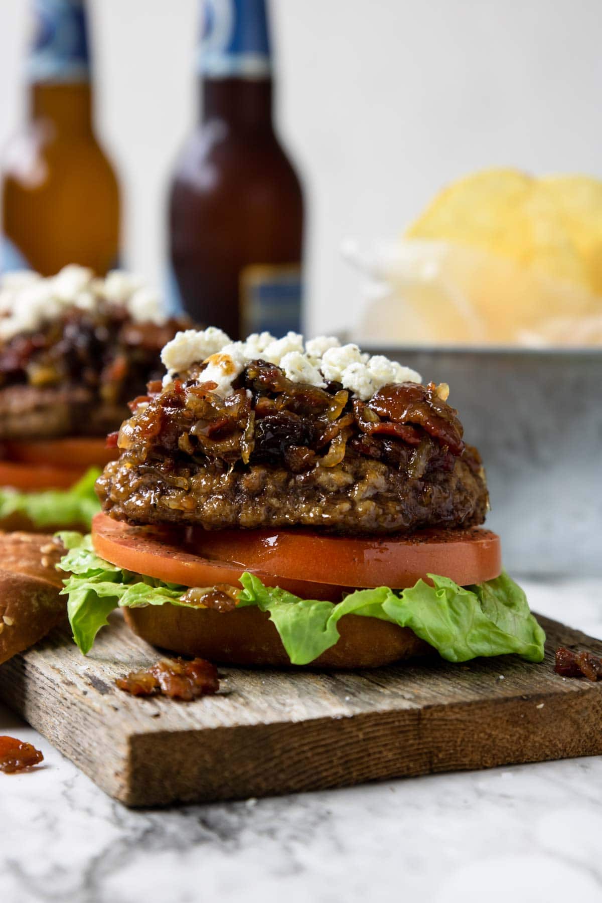 two burgers topped with bacon jam and boursin cheese and two bottles of beer in the background