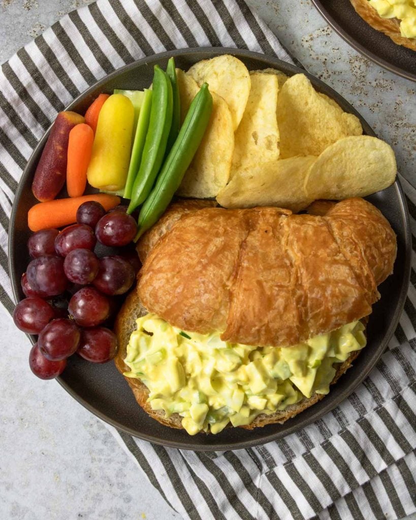 egg salad sandwich on a croissant with chips and veggies to the side
