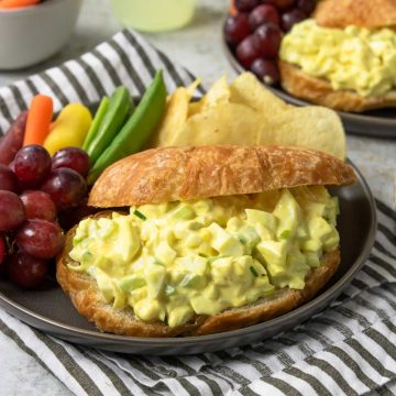 egg salad sandwich on a plate with veggies and chips