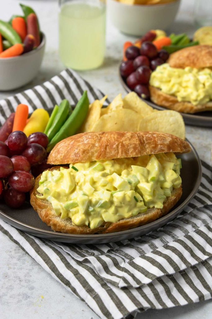 egg salad sandwich on a plate with veggies and chips