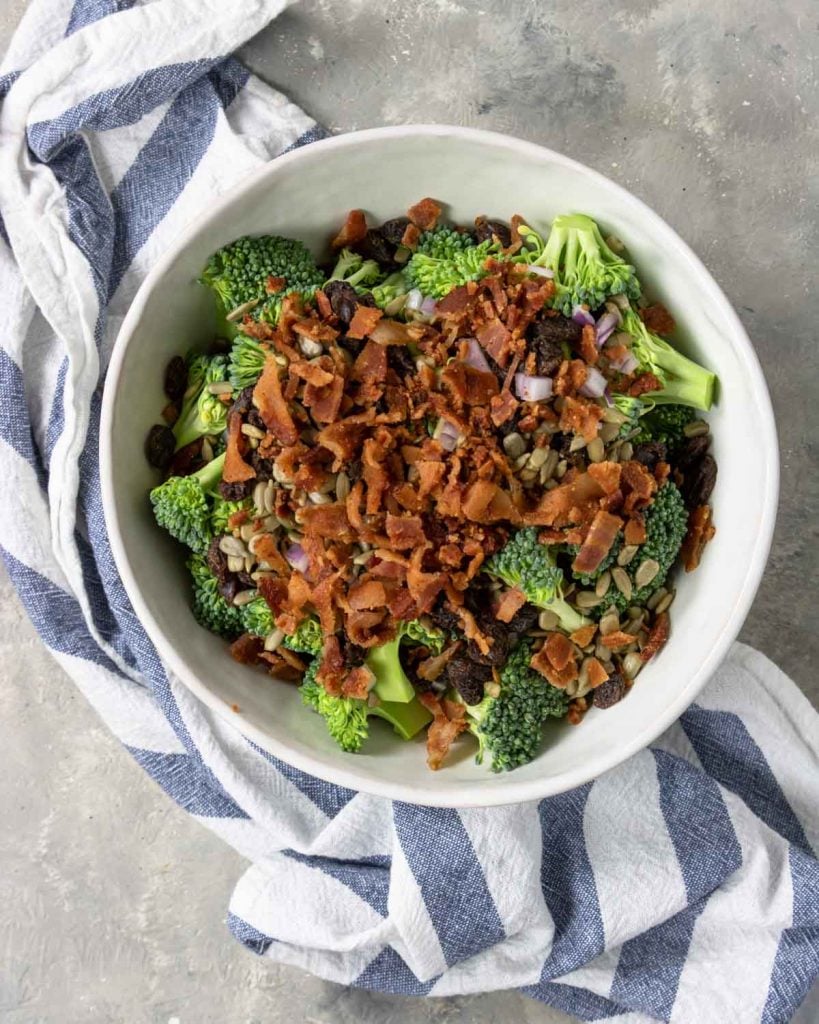 broccoli, onions, sunflower seeds and raisins in a bowl topped with bacon