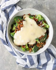 broccoli, onions, sunflower seeds and raisins in a bowl topped with bacon and mayo dressing