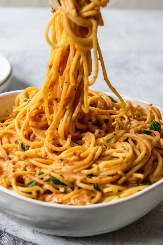 spaghetti being pulled from a bowl covered in tomato cream sauce