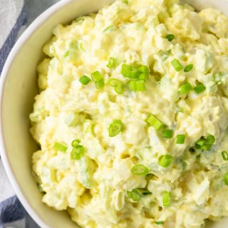 Potato salad topped with green onions in a white bowl