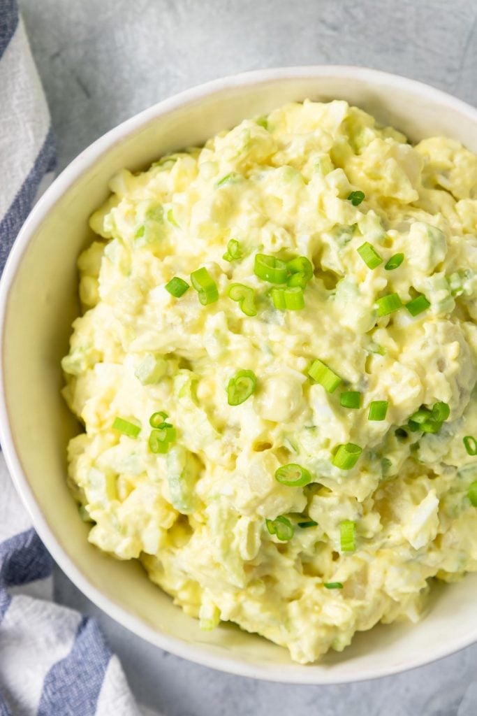 Potato salad topped with green onions in a white bowl
