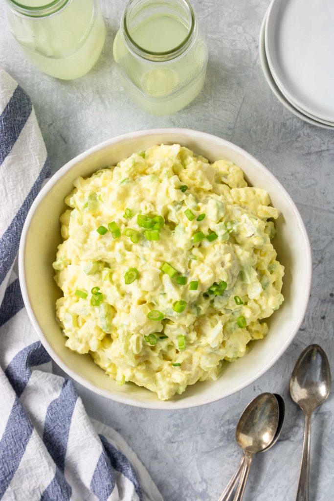 Potato Salad in a white bowl with lemonade and spoons to the side