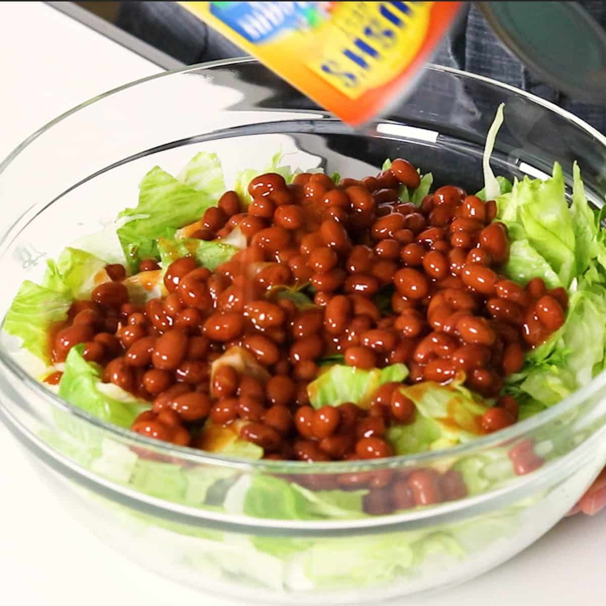chili beans in sauce being poured on top of lettuce 
