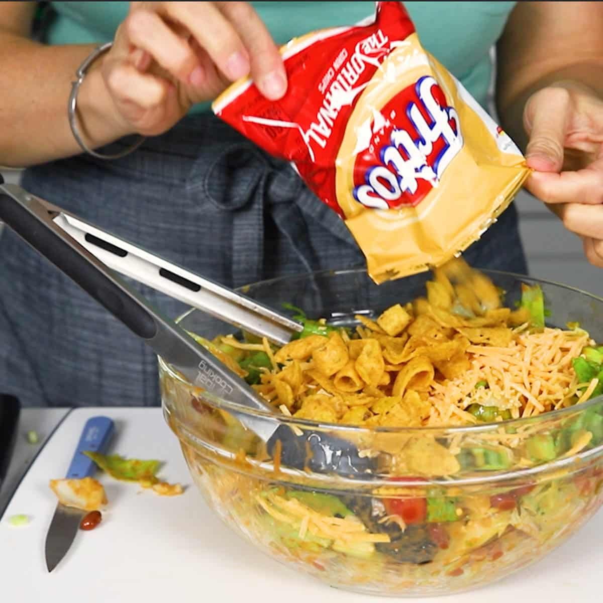 Frito Corn Chips being poured into salad bowl over salad ingredients 
