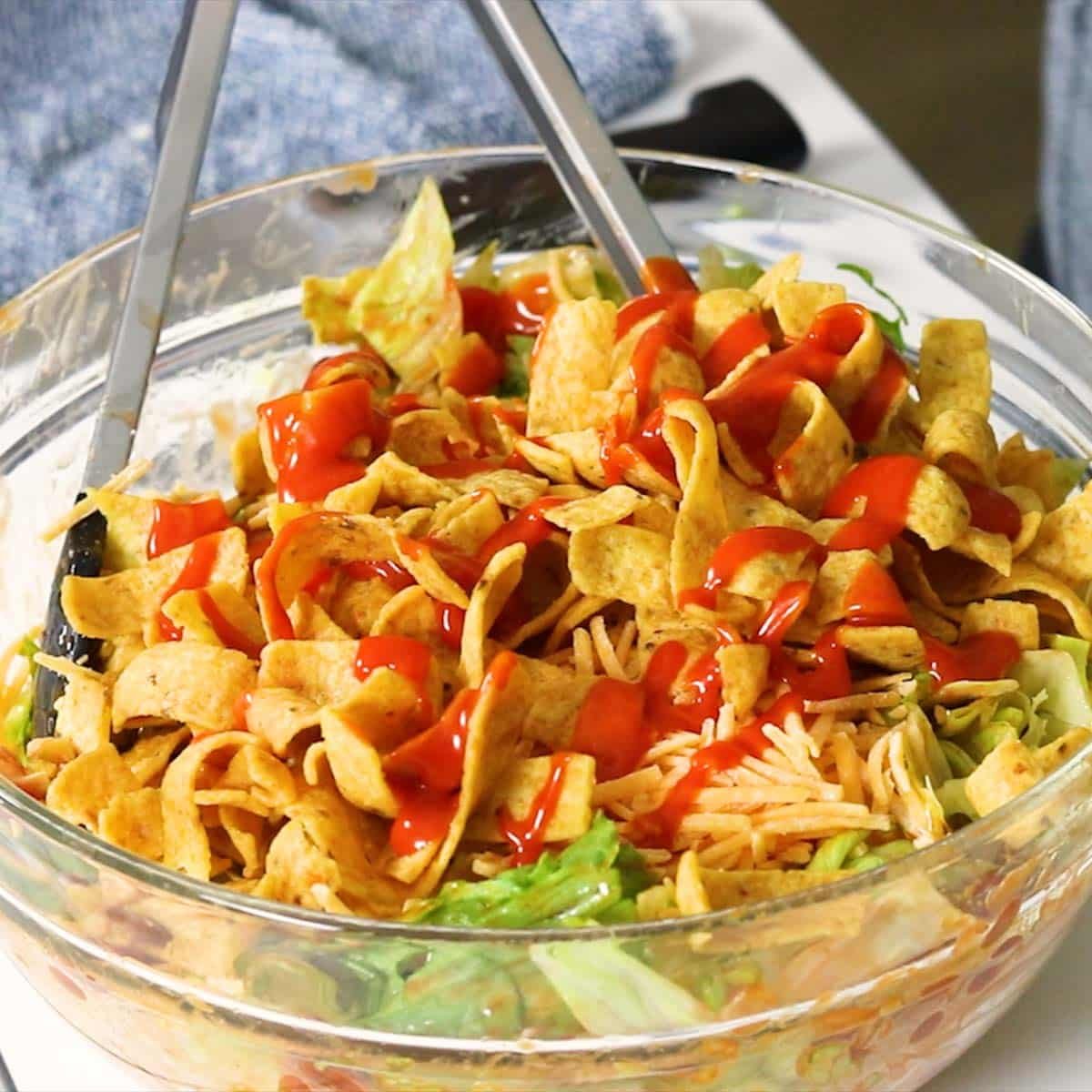 Fritos and Catalina dressing on top of a Taco salad ready to be tossed with tongs