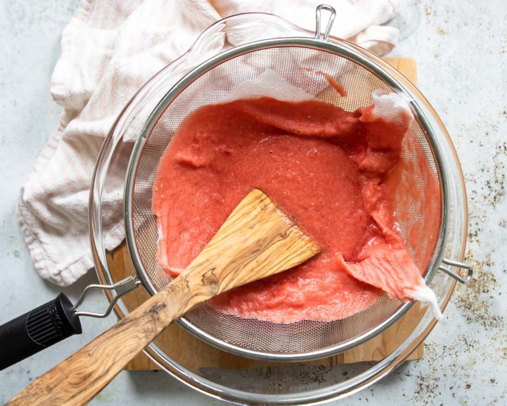 pouring blended watermelon though a fine mesh sieve lined with cheesecloth