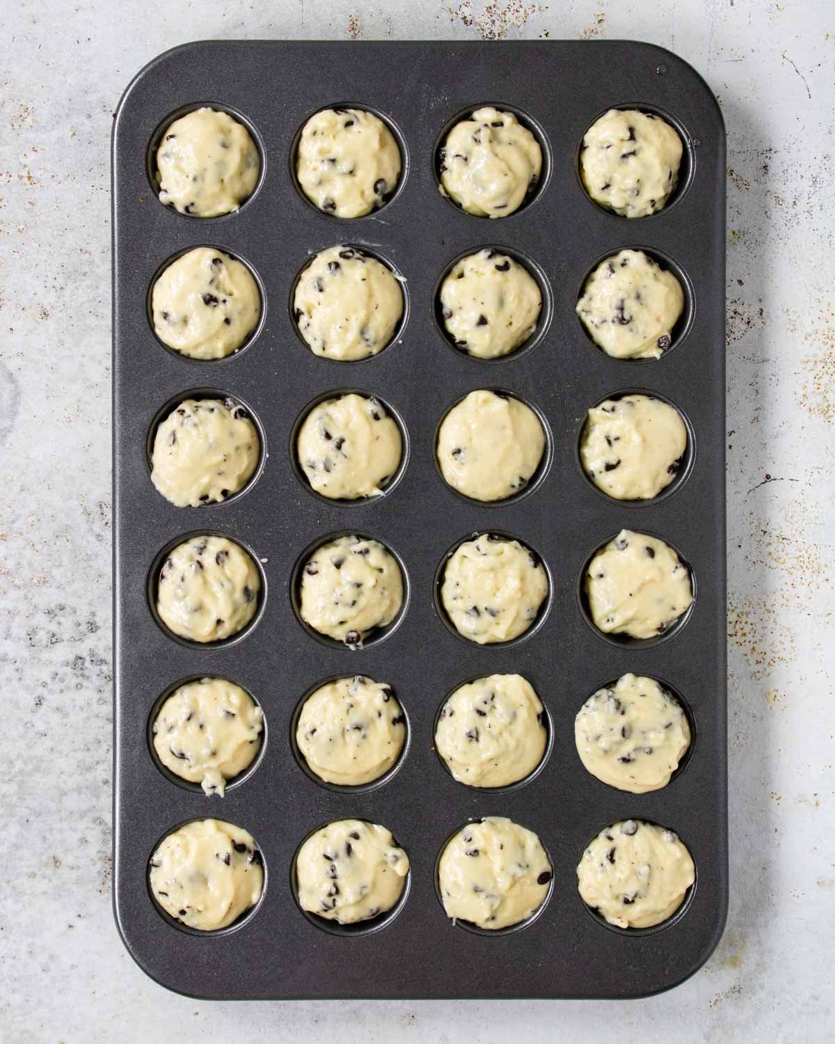 24 cup mini muffin pan filled with chocolate chip muffin batter