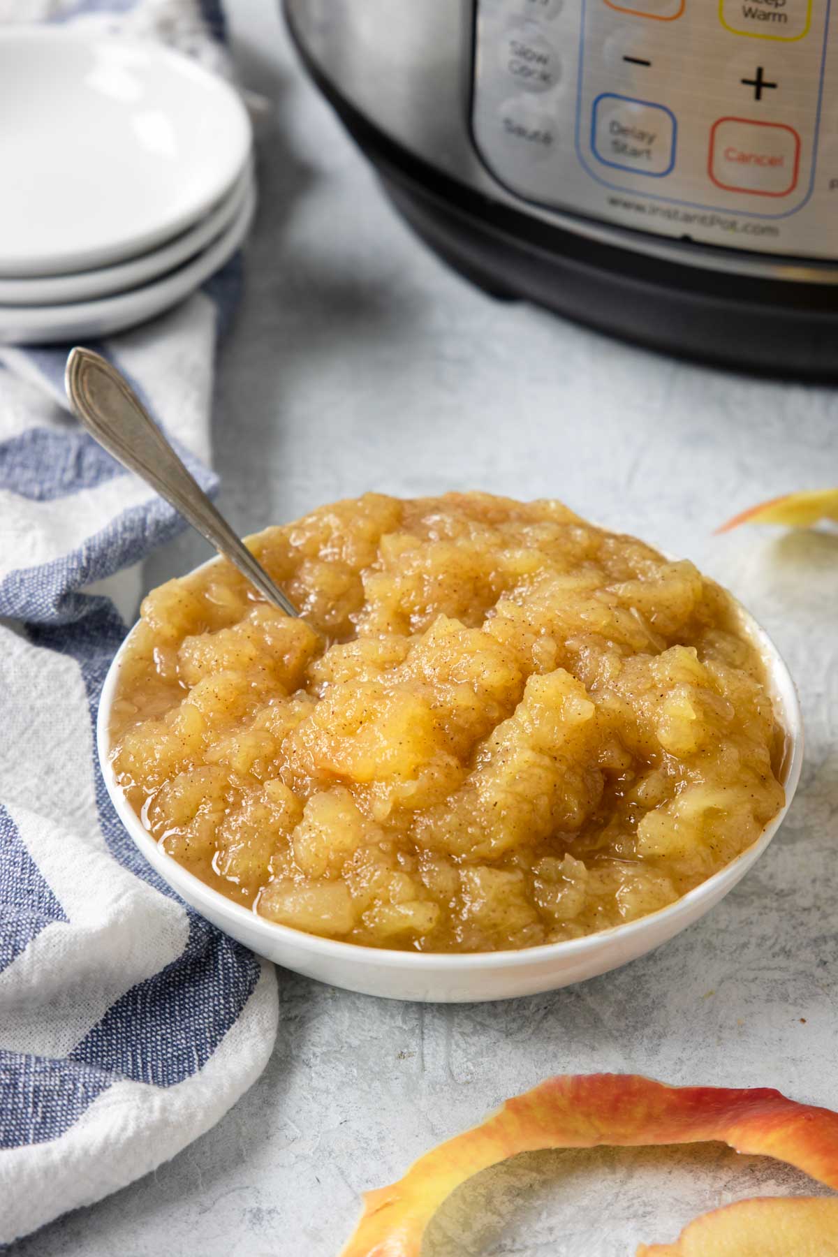 Chunky applesauce in a white bowl, Instant Pot in the backgroun