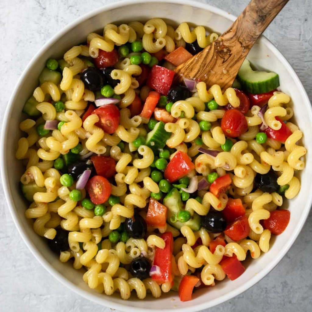 pasta salad with lots of veggies that has been all stirred together in a white bowl 