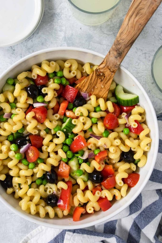 Veggie pasta salad in a white bowl with peas, black olives, tomatoes, and peppers