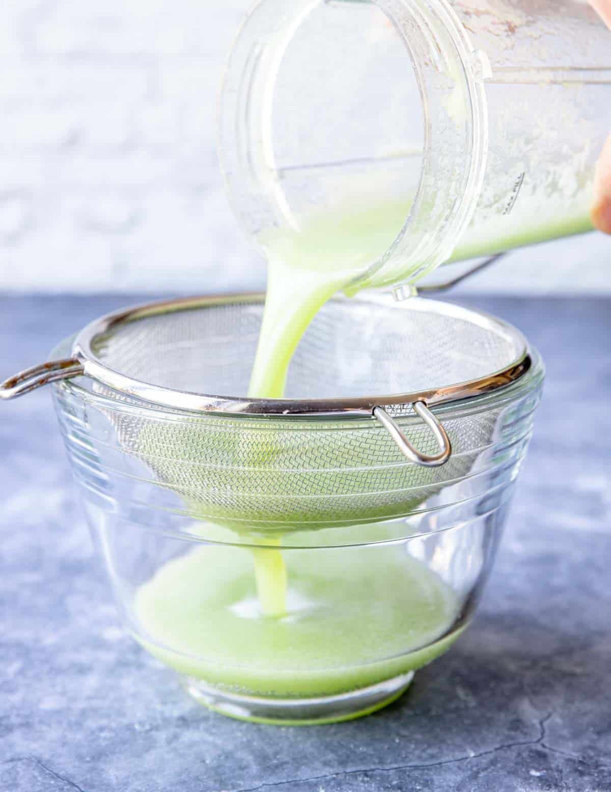 pouring pureed cucumbers through a mesh sieve to a bowl