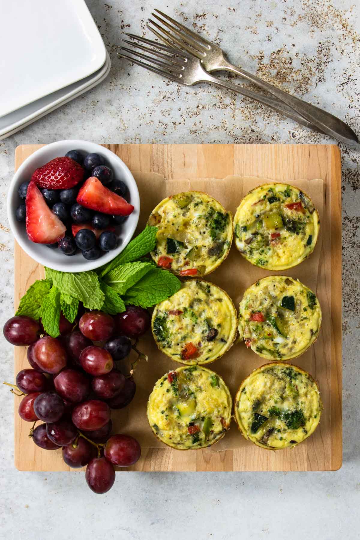 healthy breakfast egg cups on a cutting board with grapes, blueberries and strawberries