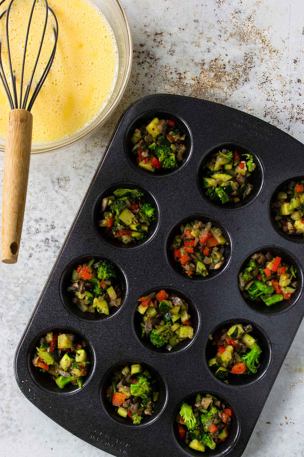 muffin tin full of veggies and an egg mixture to the side