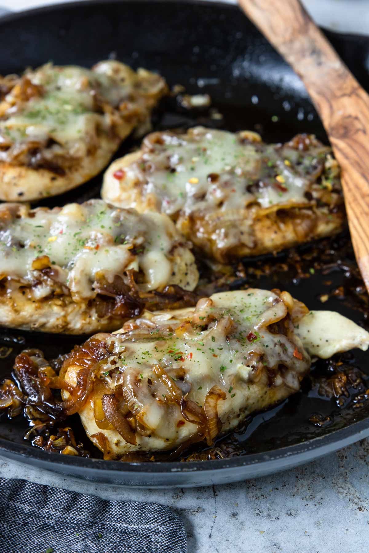 chicken breasts in a skillet that are topped with an onion jam and melted cheese