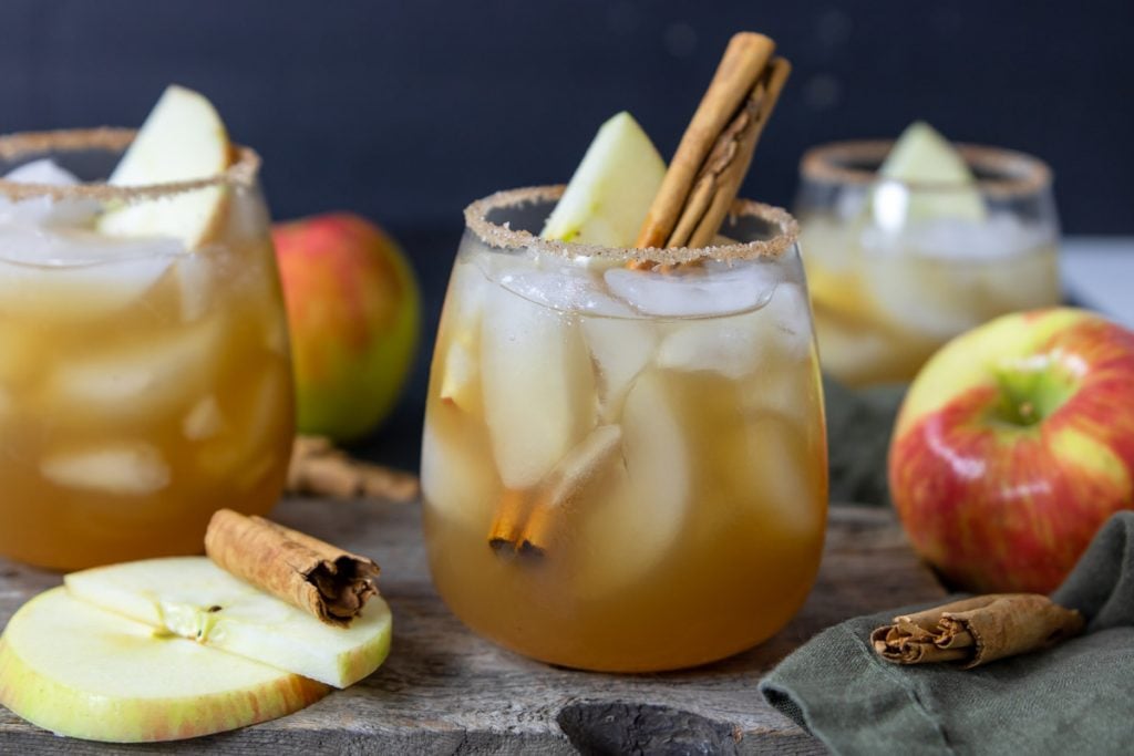 Apple Cider Margaritas in a glass with cinnamon sticks and apples