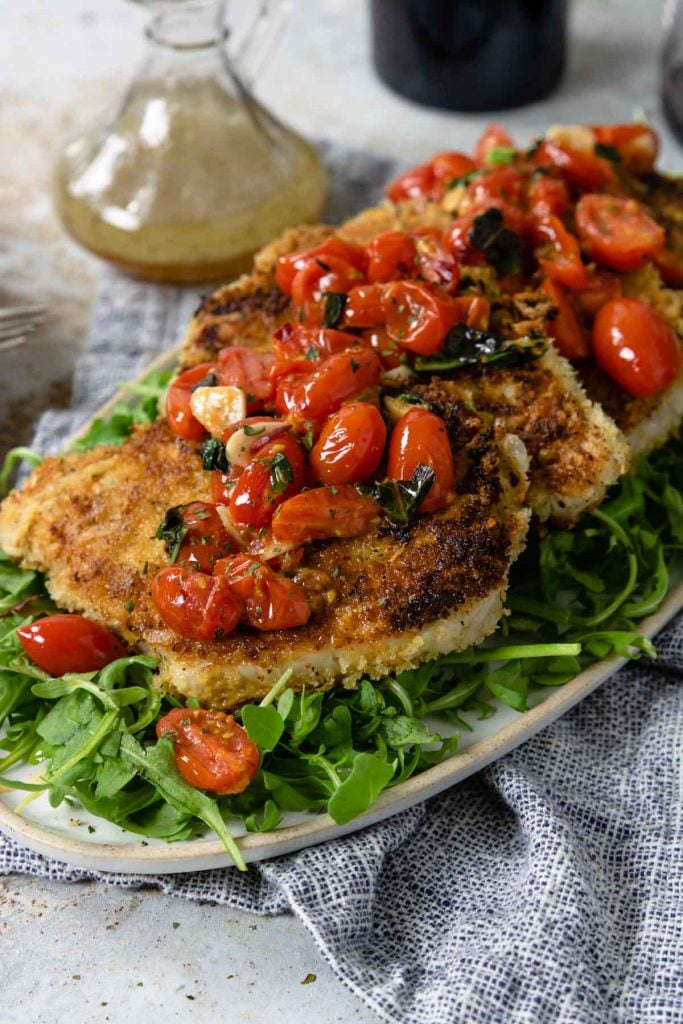 pork milanese on a platter topped with tomatoes and garlic