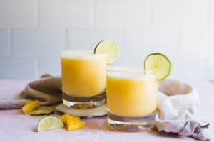 coconut pineapple margaritas in a glass with limes