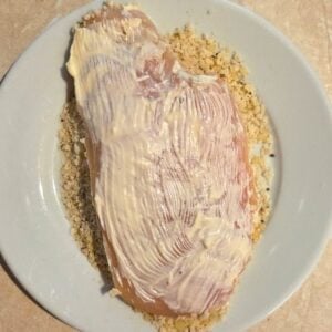 Chicken breast with mayo on a plate of seasoned bread crumbs