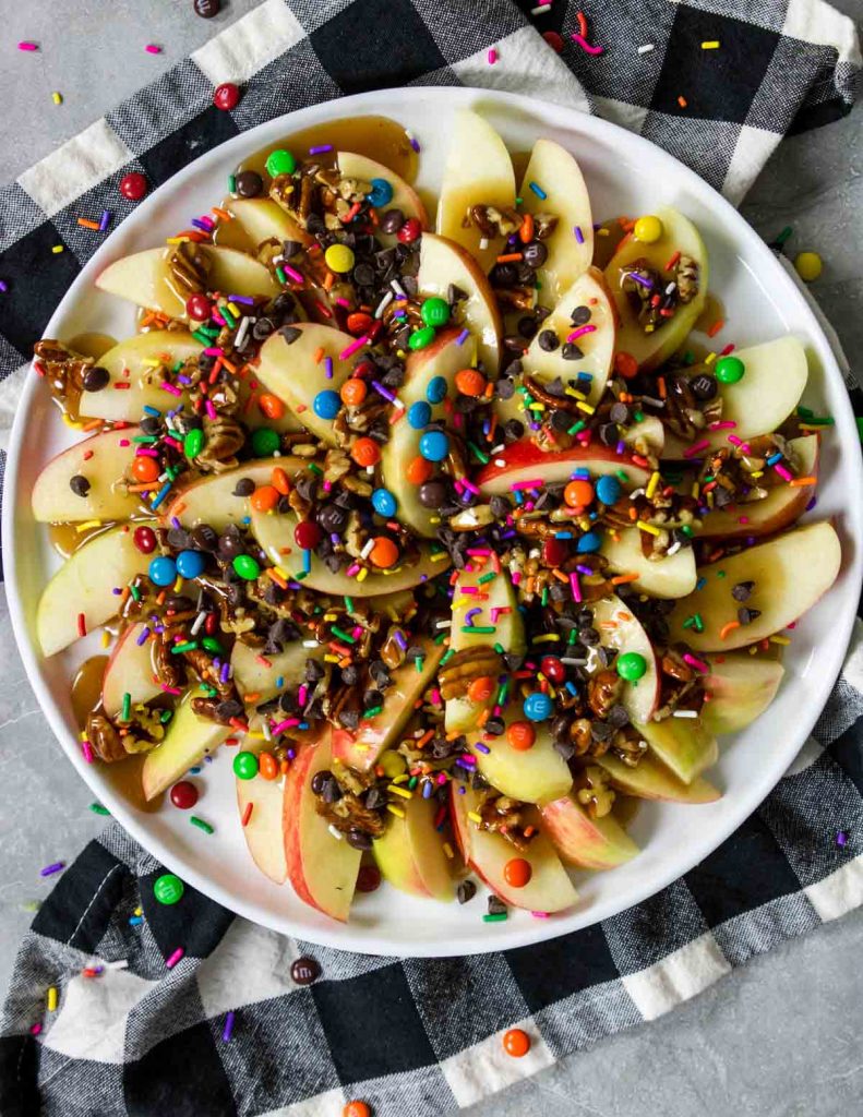 plate of apple nachos topped with caramel sauce, pecans,  sprinkles and chocolate chips 