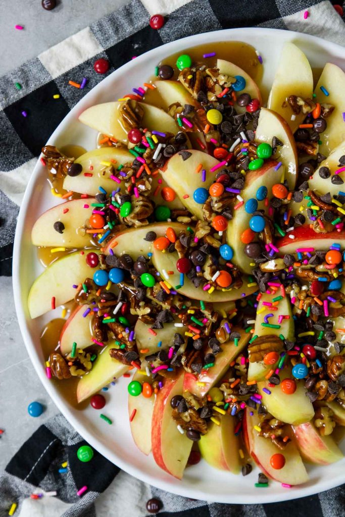 apples on a plate topped with caramel, pecans, chocolate chips and sprinkles