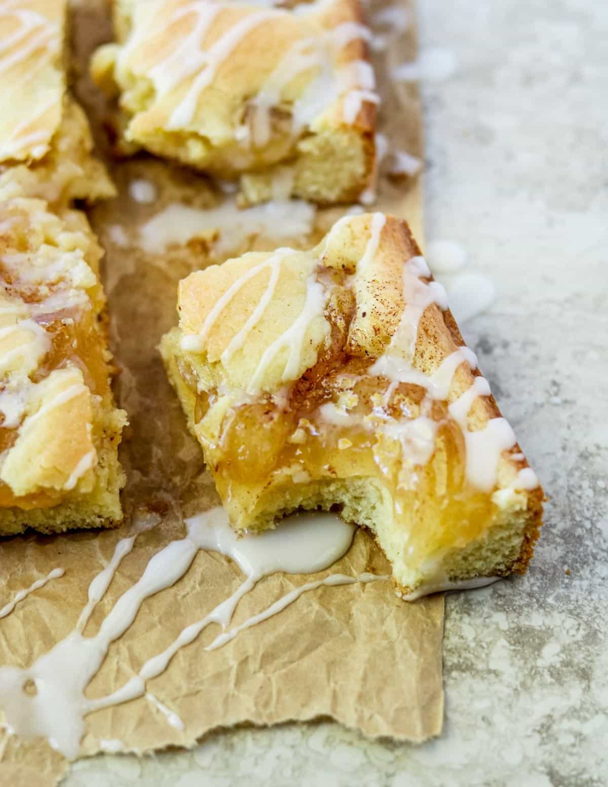 Apple Pie Bars cut into rectangles and placed on a sheet of parchment paper, drizzled with powder sugar glaze