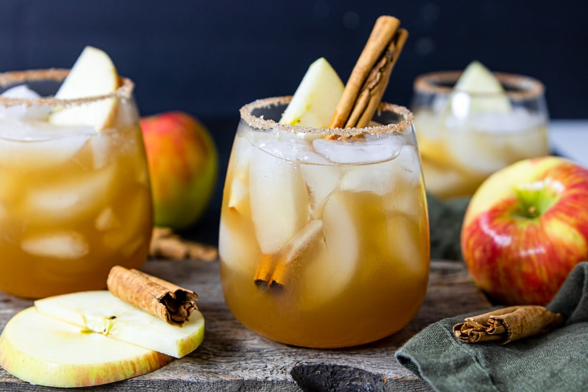 Apple Cider Margaritas in a glass with cinnamon sticks and apples