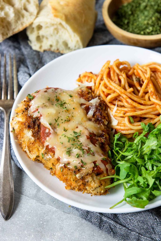 A plate with chicken parmesan, salad and spaghetti