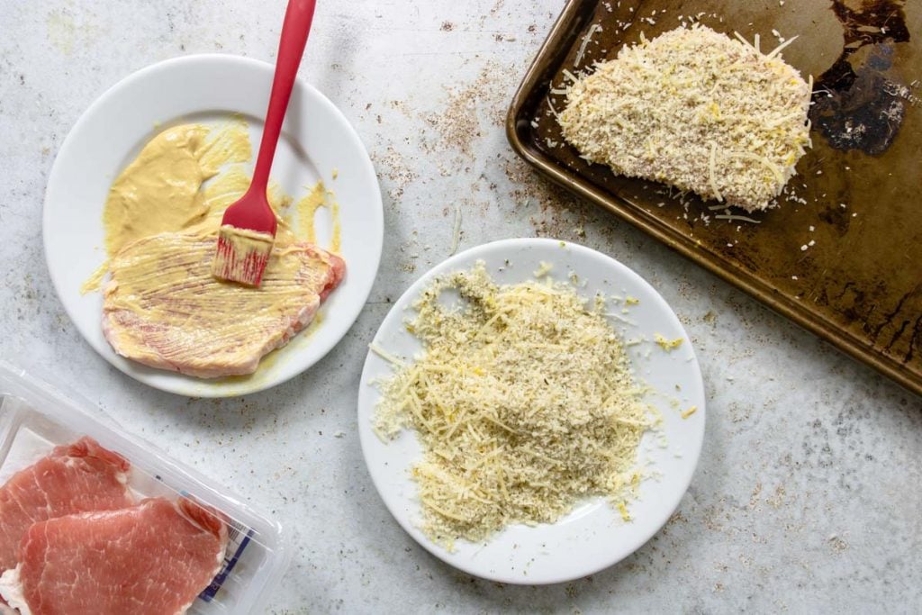 raw pork cutlets, a plate of dijon mustard, and a plate of panko for breading pork milanese