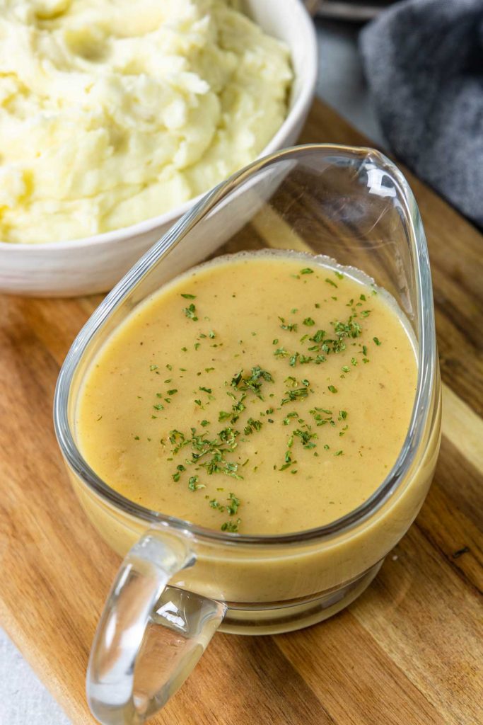 a glass boat of gravy garnished with parsley and a bowl of mashed potatoes