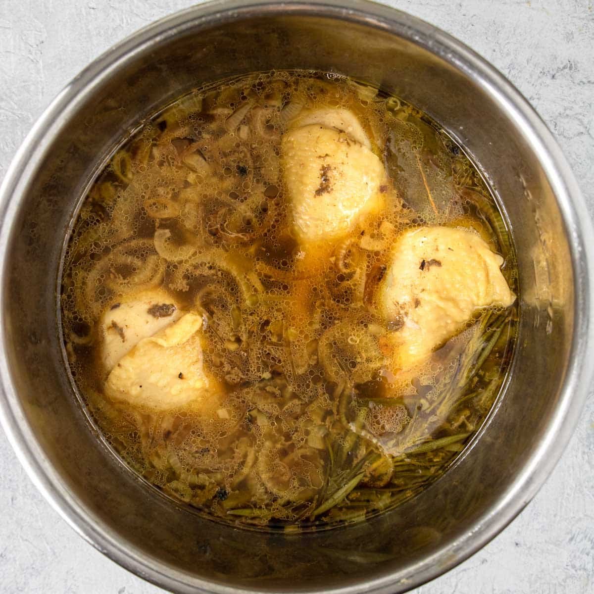 chicken legs and chicken broth in the instant pot with onions and aromatics