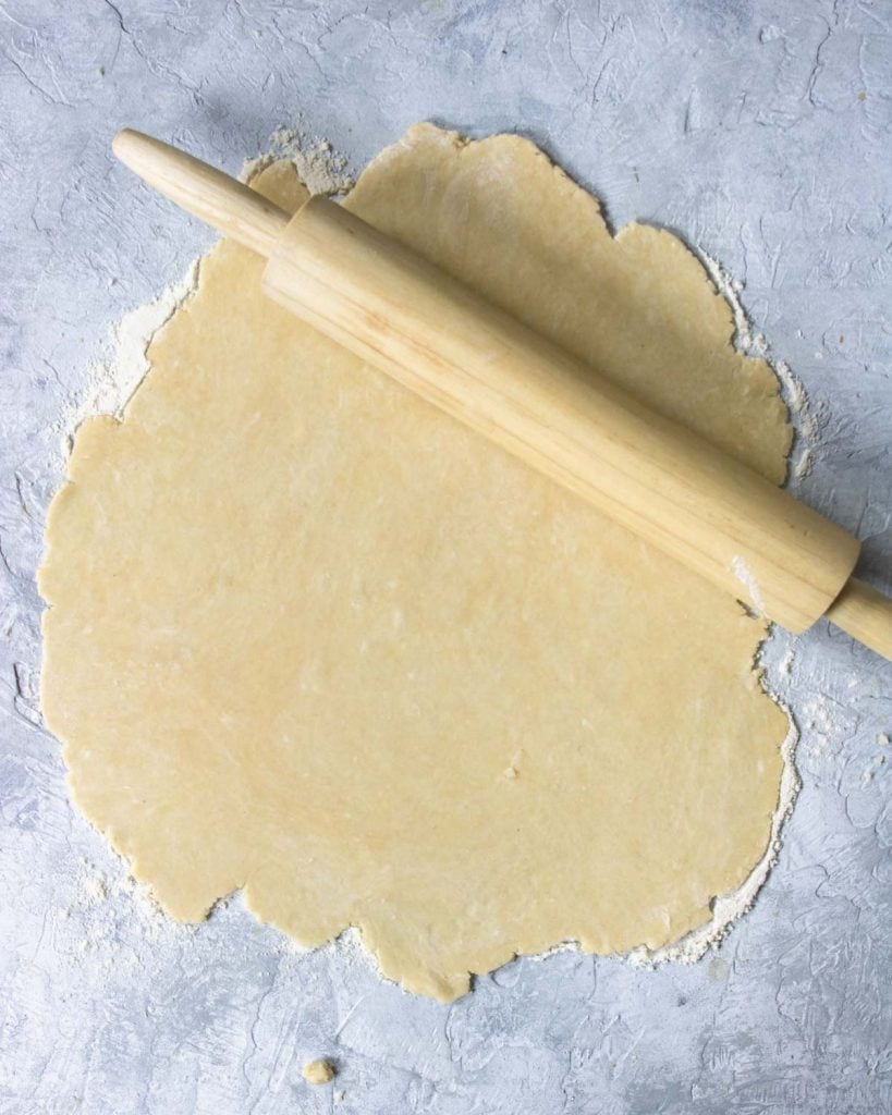 pie crust being rolled out on a floured surface with a wooden rolling pin
