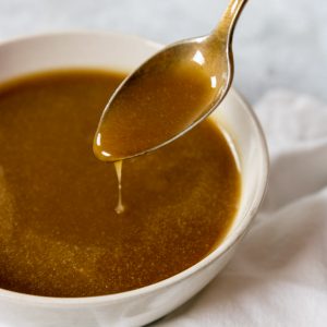 brown sugar caramel sauce in a white bowl being drizzled with a spoon