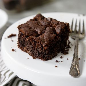 one brownie on a cake plate with crumbs around and a fork