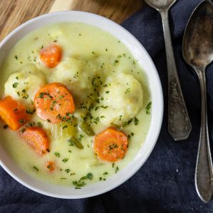 chicken and dumplings in a white bowl with two spoons