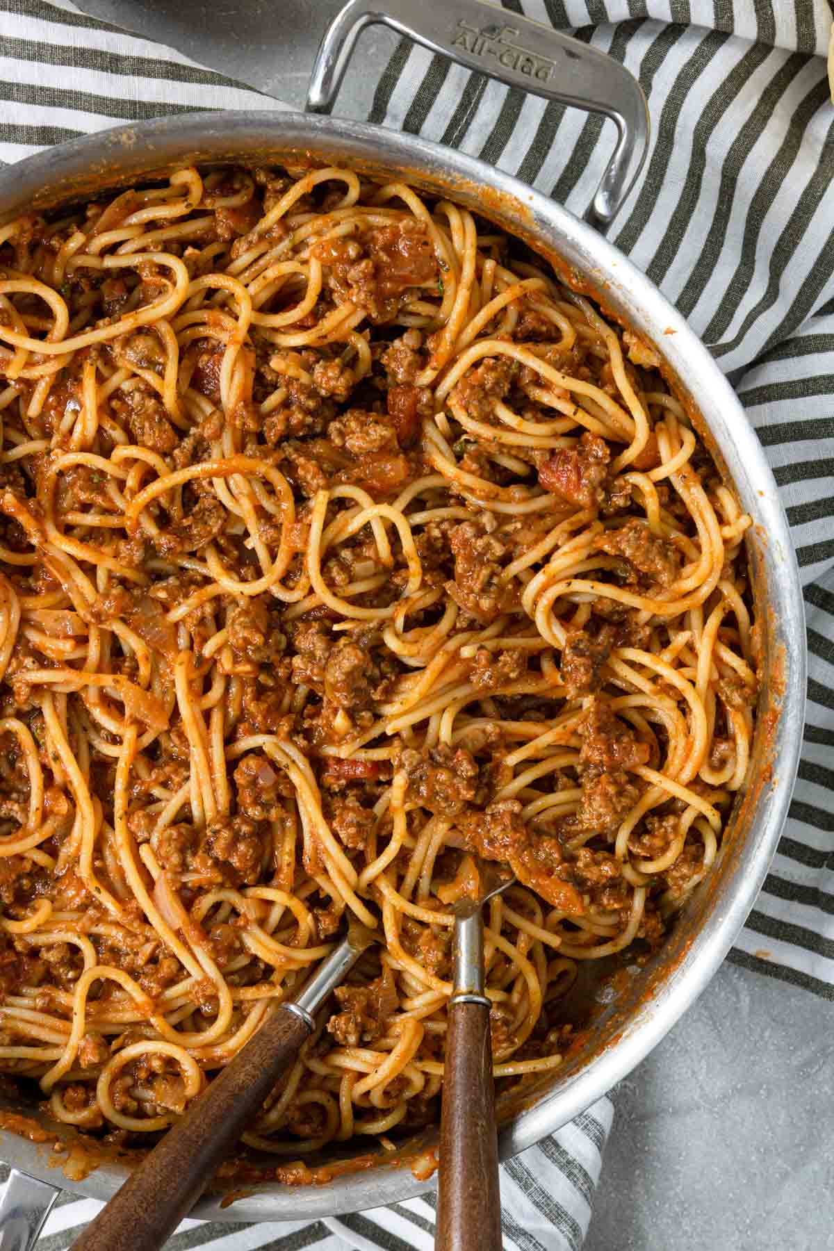 spaghetti that has been tossed with a meat sauce, in a skillet with two forks