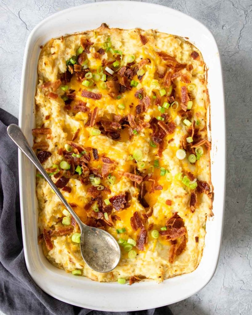 twice baked potato casserole in a white baking dish with a serving spoon