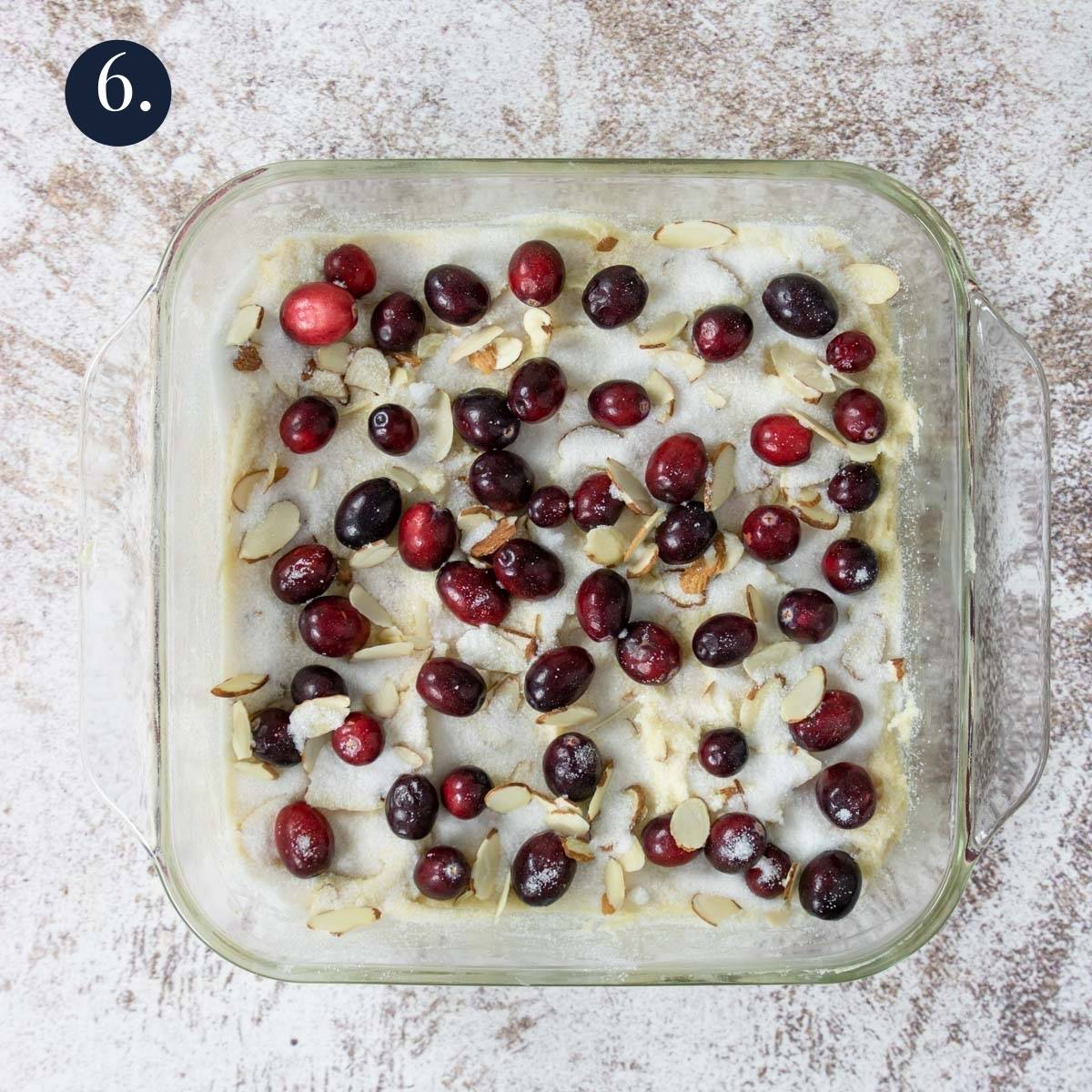 cake batter in an 8x8 with cranberries, almonds and sugar on top