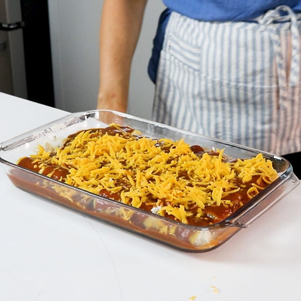 Cheese on top of enchiladas with enchilada sauce, ready for the oven