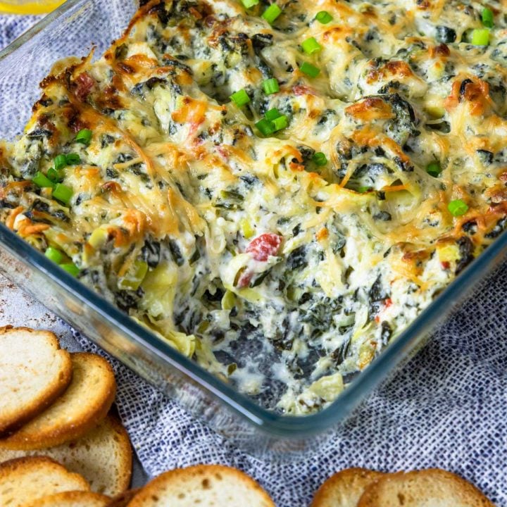spinach artichoke dip in a baking dish with a scoop taken out