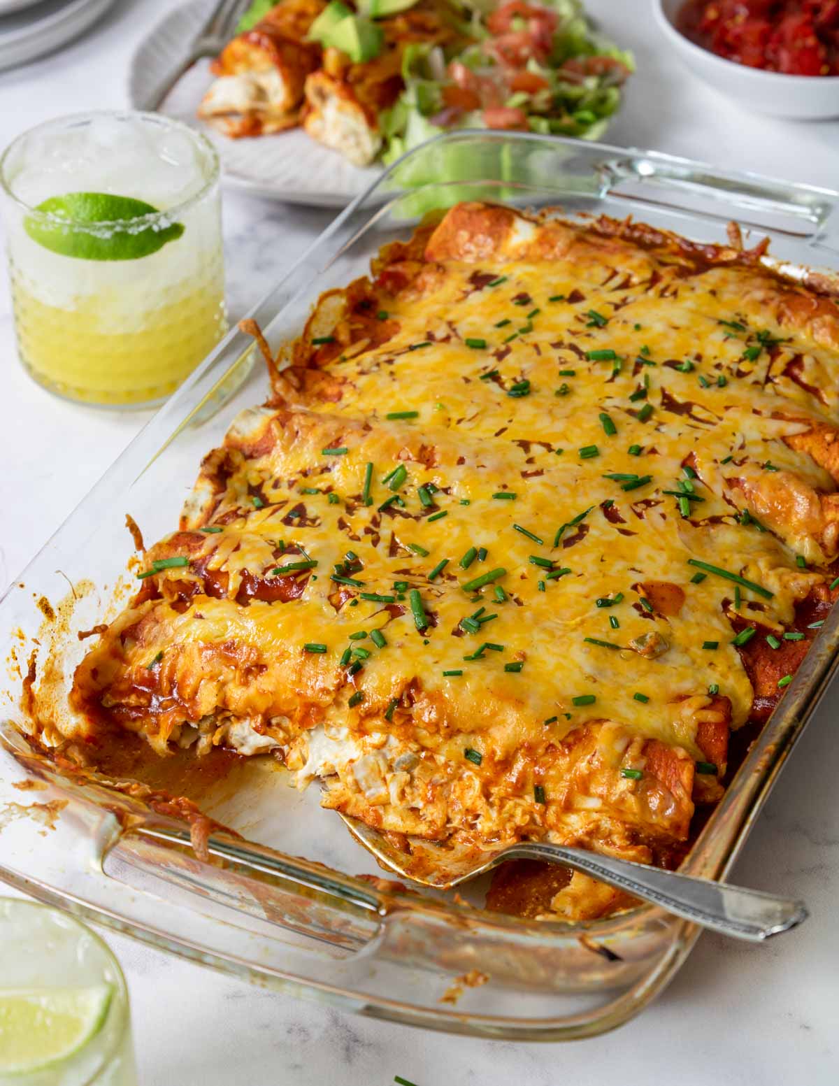 cream cheese chicken enchiladas baked in a glass casserole pan with margaritas in the background