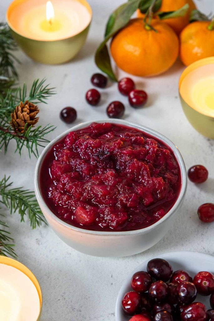 Cranberry sauce in a white bowl with fresh cranberries and oranges around
